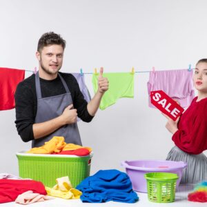 Front view young couple man giving thumbs up his wife holding sale sign clothes rope white wall